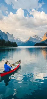 Canoeist paddling on a reflective mountain lake under a bright sky with distant peaks.