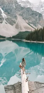 Woman on log overlooking mountain lake with turquoise water.