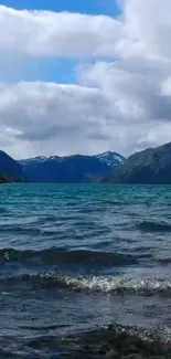 Tranquil mountain lake with blue water and surrounding peaks under a cloudy sky.