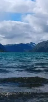 Scenic lake with mountains and clouds under a blue sky.