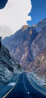 Mountain road under blue sky with rocky peaks.