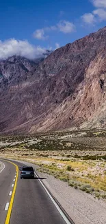 Car journeying through vast mountain landscape under blue sky.