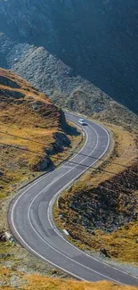 A car drives down a winding road through scenic mountain terrain under blue skies.