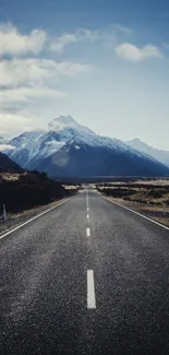 Scenic road leading to snowy mountains under a bright blue sky.