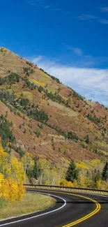 Scenic mountain road in autumn with clear blue sky and vibrant fall colors.