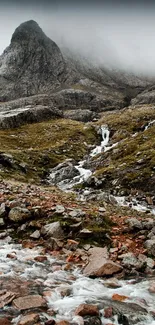 Mountain stream flowing through rocky terrain under misty peaks.