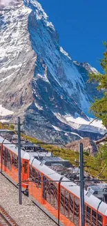 Red train traveling through scenic snowy mountains with blue skies.