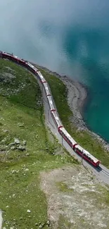 A train curls beside a blue lake in a lush green mountain landscape.