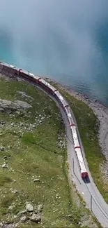 Aerial view of a red train winding through green mountains beside a blue lake.