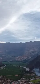 A wide view of a serene mountain valley with a river and cloudy sky.