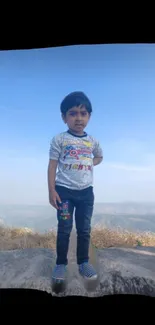 Child standing on mountain with blue sky background.