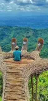 Man sitting on bamboo platform overlooking lush green hills.