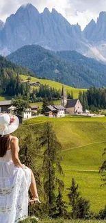 Woman in white dress overlooking mountain village and lush green landscape.