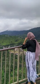 Person overlooking scenic green mountains under cloudy sky.