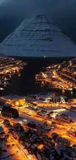 Aerial view of a snowy mountain village at night, illuminated by warm lights.