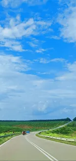 Scenic open road under a vibrant blue sky with lush green fields.