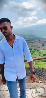 Stylish man posing in scenic outdoor landscape with green hills.