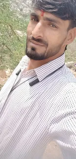 Man taking selfie outdoors with trees and rocky terrain.