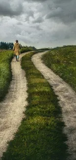 A solitary figure walks along a winding path in a green landscape under a cloudy sky.