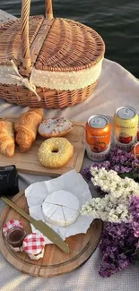 Picnic scene with basket, pastries, and flowers by a lakeside.