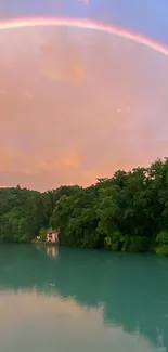 Rainbow arches over a lake with lush greenery and vibrant sky at sunset.