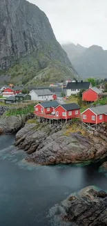 Red cabins by rocky waters with mountain backdrop.