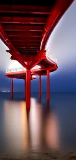 A red pier extends over calm water under a midnight blue sky.