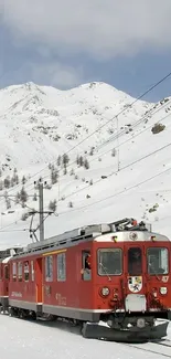 Red train traveling through snowy mountain landscape.