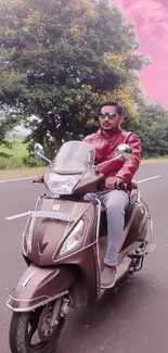 Man riding a scooter on a scenic road with pink skies.