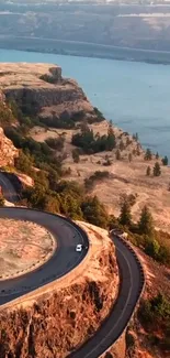 Aerial view of a scenic winding road along a sandy river cliff with lush greenery.