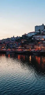 Riverside cityscape at dusk with lights reflecting on water.