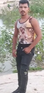 Man standing by a river with floral greenery and rocky banks.