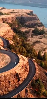 Aerial view of a winding road along stunning cliffs beside a tranquil river.