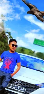 Man with sunglasses leaning on a car with a bird flying overhead.