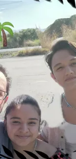 A family selfie on a sunny roadside with a scenic backdrop.