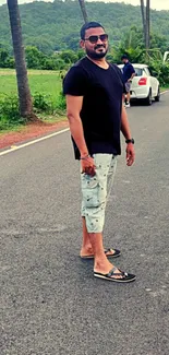 Man strolling on a scenic roadside with lush green backdrop and relaxed vibe.