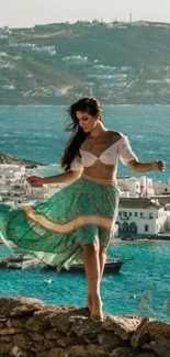 Woman dancing by the turquoise sea with a coastal town backdrop.