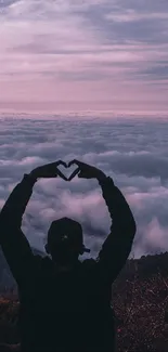 Silhouette forming a heart against a pink and purple cloudy sky over mountains.