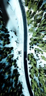 Aerial view of snowy road through green forest.