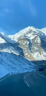 Scenic road through snow-capped mountains under a vibrant blue sky.