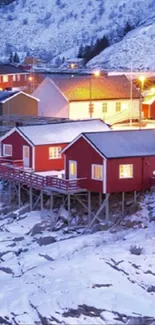 Snowy village with red cabins at night with glowing lights.