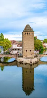 Strasbourg tower reflection in calm river under blue sky.