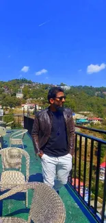 Man on scenic terrace with blue sky and green hills.