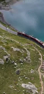 Aerial view of a train passing by a blue lake surrounded by green hills.