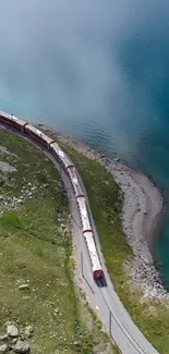 A scenic train passes a tranquil blue lake with mountainous backdrop.