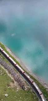 A scenic train by a turquoise lake surrounded by greenery.