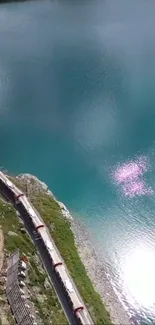 A train winding by a stunning turquoise lake under a clear sky.