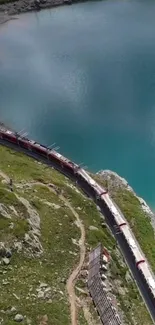 Red train curving by a turquoise lake surrounded by green landscape.