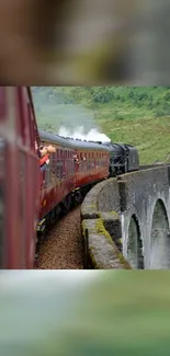 Steam train crossing a scenic green valley bridge.