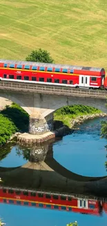 Red train crossing stone bridge over a river with lush greenery.